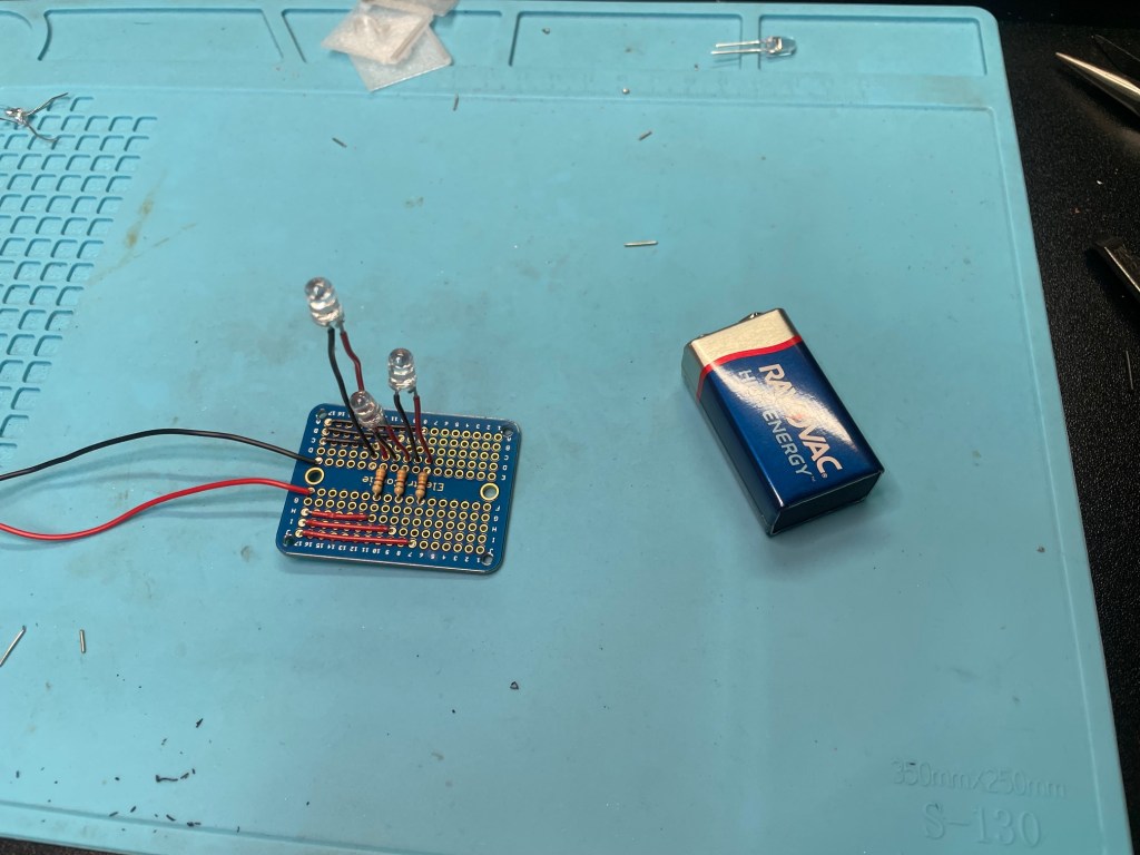 A circuit board on a silicone mat next to a 9 volt battery